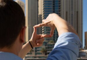The man looks at the buildings and makes a frame of his fingers